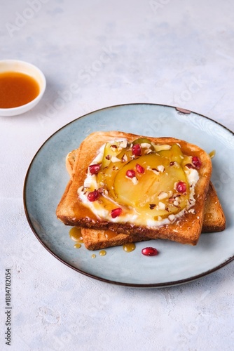 Toast with caramelized pear, ricotta, and hazelnuts on a ceramic plate against a light concrete background.