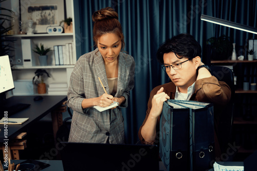 Serious face of manager with coworker discussing overworked folder paper at over late night, writing check list memo of collected signing document for board company keeping database file. Infobahn.