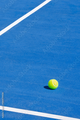 Tennis ball on a blue outdoor court with clean lines and natural light.