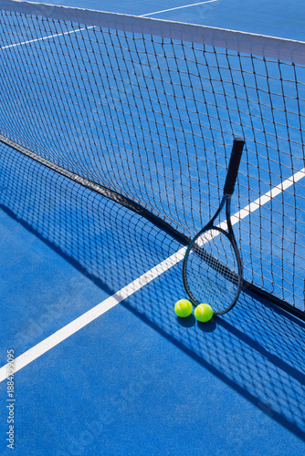 Bild auf Leinwand Tennis balls and a racket leaning against the net on a blue outdoor tennis court