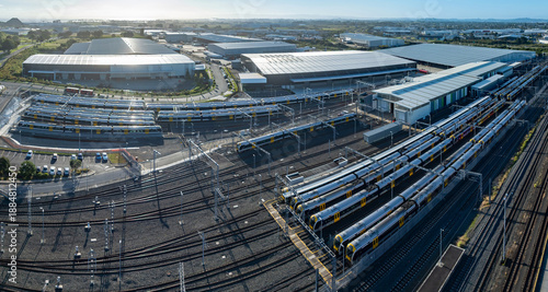 Aerial view of train depot in Auckland, New Zealand. Rows of electric trains are parked on tracks for maintenance and storage. The depot supports public transportation.
