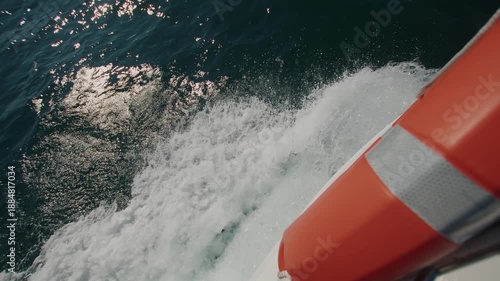 Aerial view of seething water with white foam near side of yacht with a lifebuoy and surface of the blue sea sparkling in sun. Close-up