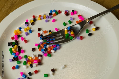 Colorful beads spread across a white dinner plate with a fork, illustrating the invisible threat of plastics in food.