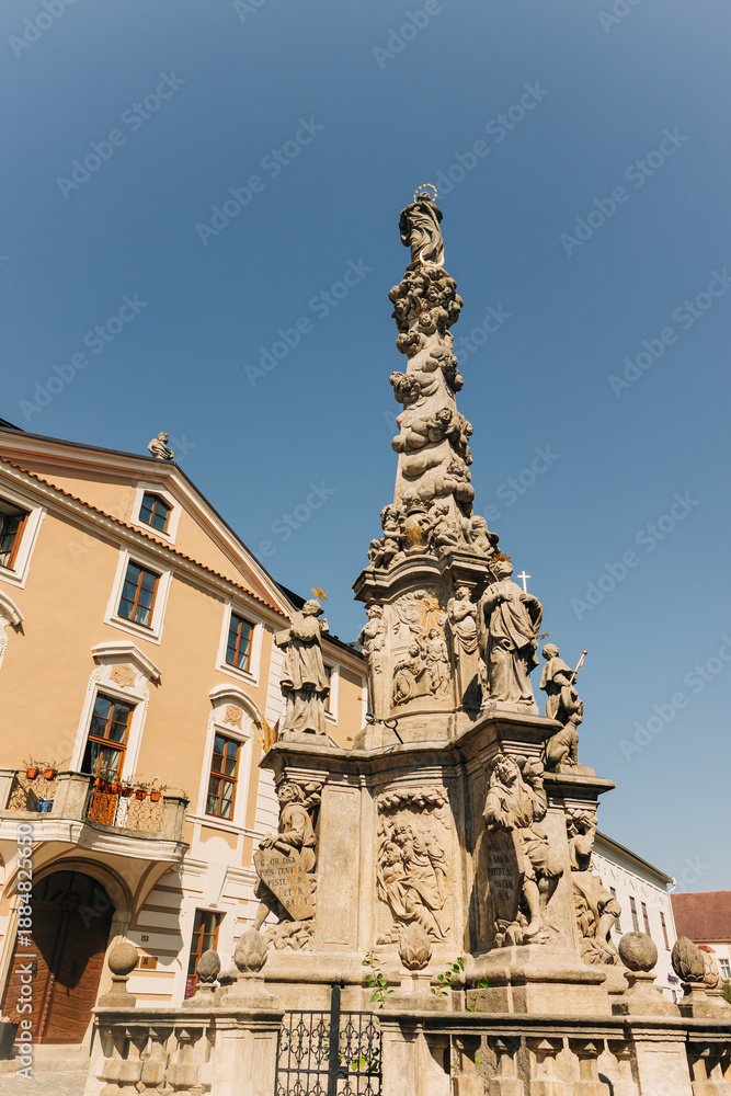 Fototapeta premium Historical fountain in a public square of an old european city of Kutna Hora in Czech Republic surrounded by old buildings under a clear blue sky