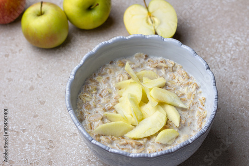 Multigrain cereal porridge made from rye, oats, barley, buckwheat and wheat flakes, served with milk and fresh apple slices. Neutral stone background, soft daylight, healthy breakfast concept