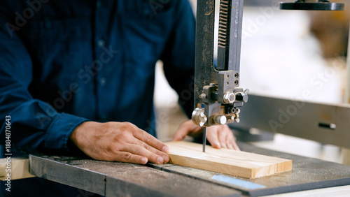 Slika na platnu Skilled carpenter pushing a wooden board through a bandsaw, shaping material in