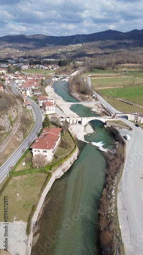 Cinematic vertical drone footage of Tanaro River with ancient Roman bridge and Bagnasco city on the left bank and old mill on the right bank captured on a sunny winter day 2