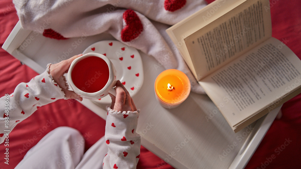 Fototapeta premium Cozy morning with a book, hot drink, and a candle, decorated with hearts