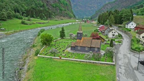 Wallpaper Mural Drone view flying above Flam kyrkje near the river in Norway. Aerial footage highlights wooden church, cemetery and surrounding countryside in summer. Torontodigital.ca