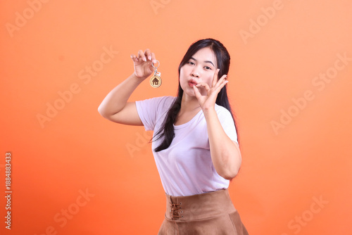 Young woman holds the house keys and shows a symbol of okay with her hand, presenting a new home and happiness. isolated on orange background