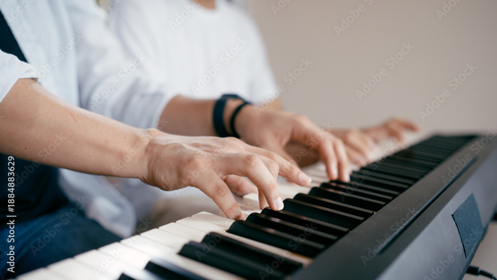 Fototapeta premium Two people playing an electric piano keyboard, focusing on their hands pressing the keys, indicating music education and learning