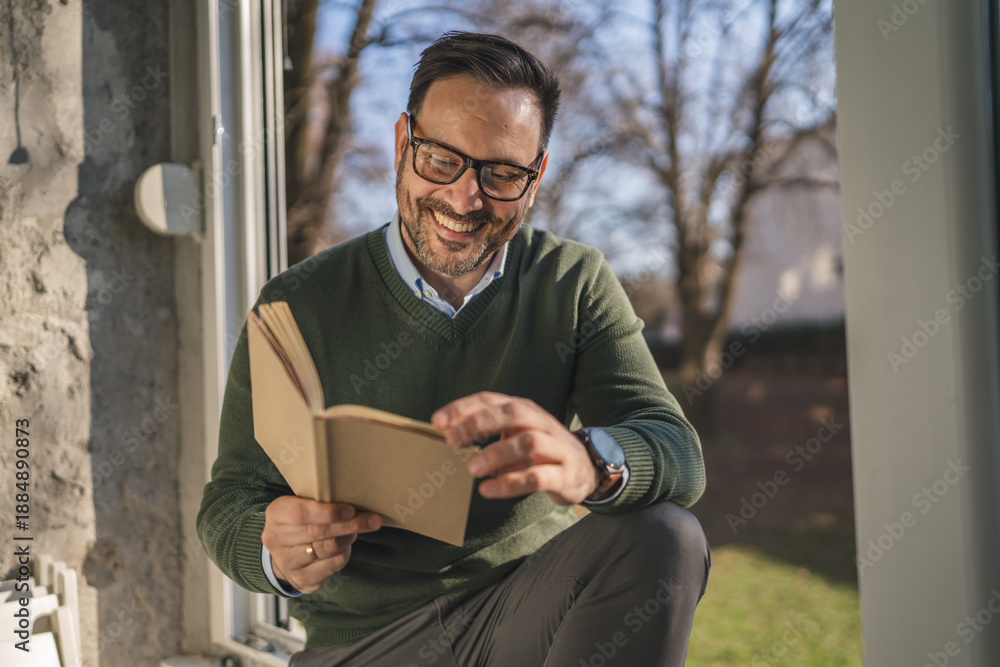 Fototapeta premium Man enjoying leisure time while reading book by window