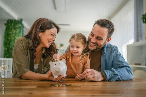 Fotografie Family teaching child about saving money with piggy bank