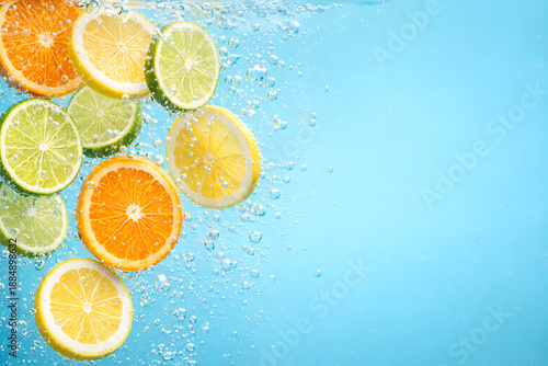 Vibrant and refreshing slices of orange, lemon, and lime citrus fruits elegantly falling into clear blue water, surrounded by effervescent bubbles, symbolizing freshness and healthy hydration.