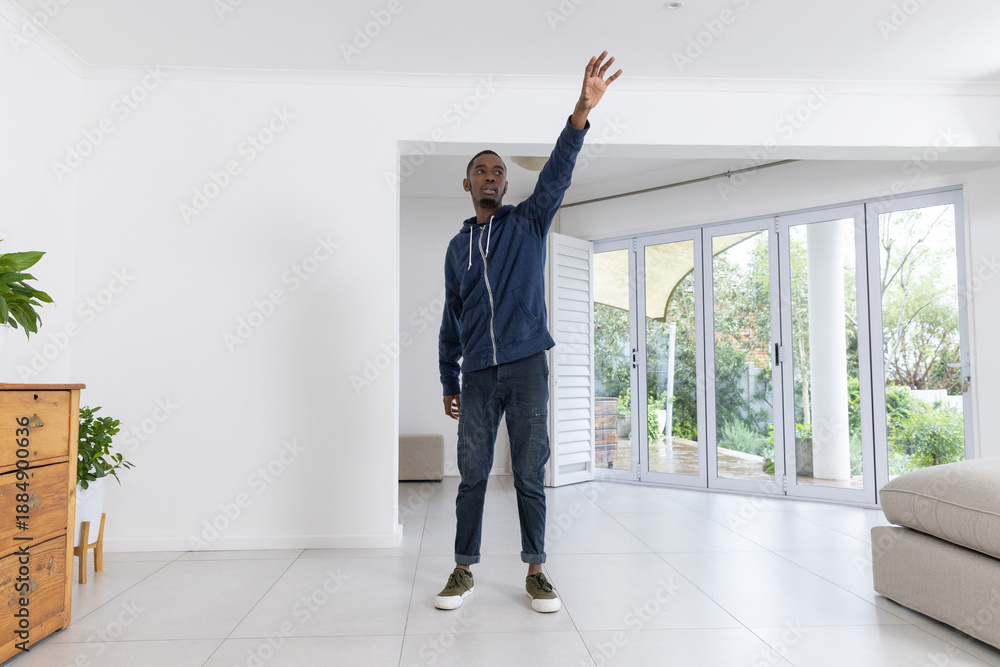 Naklejka premium African American man in 20s standing in living area reaching upward toward glass doors