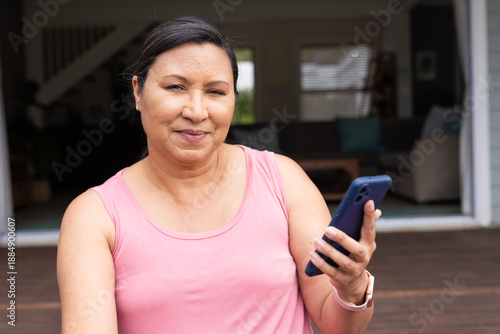 Mature female sitting on deck holding blue phone by open door, wearing pink top and smartwatch