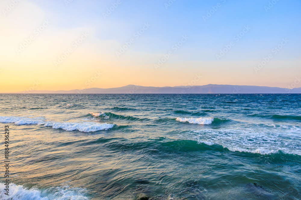 Obraz premium Tranquil sunset on the mediterranean sea with gentle waves and distant mountains