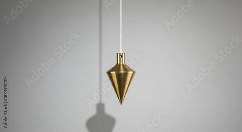Brass plumb bob hanging on white string with shadow on gray background gold metal tool