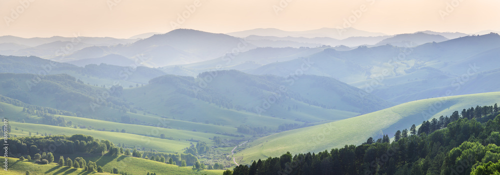 Fototapeta premium Ridge gradients in haze, panoramic view of the summer evening, hills and mountain slopes in sunset light