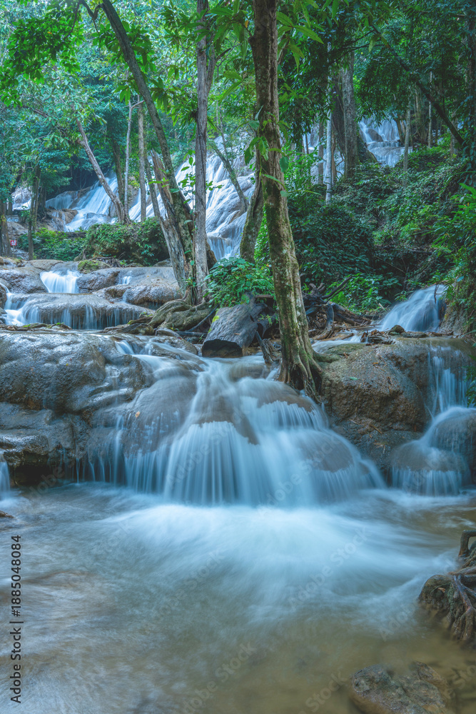 Obraz premium Beautiful horizontal landscape of a tiered limestone waterfall flowing through a lush green tropical forest. Serene nature scenery with silk water effect and trees framing the cascading stream.