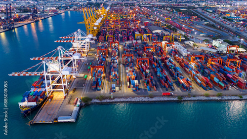 Wallpaper Mural a busy cargo container terminal port illuminated at night. Industrial logistics landscape with gantry cranes loading shipping vessels during twilight blue hour. Global trade infrastructure concept. Torontodigital.ca