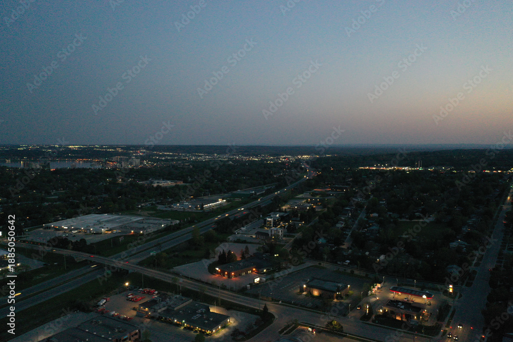 Fototapeta premium Aerial view of barrie, ontario, at dusk, showing residential and commercial areas, a highway with vehicle light trails, and the glowing city skyline along kempenfelt bay on lake simcoe