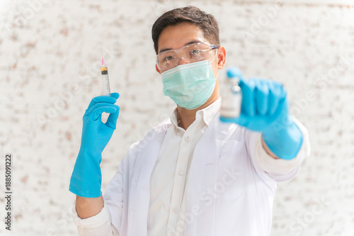 Doctor in white coat holding syringe with vaccine ready for injection and blue protective gloves, holds a syringe ready for an injection