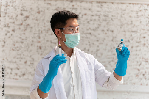 Doctor in white coat holding syringe with vaccine ready for injection and blue protective gloves, holds a syringe ready for an injection
