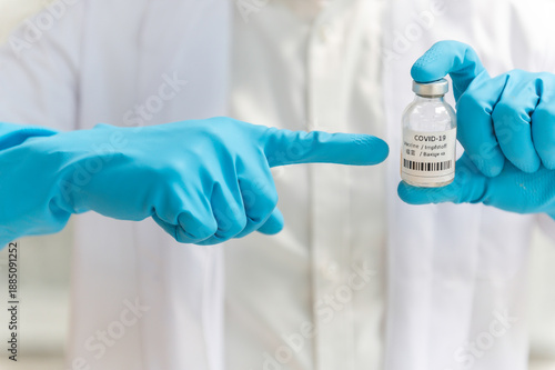 Doctor in white coat holding syringe with vaccine ready for injection and blue protective gloves, holds a syringe ready for an injection