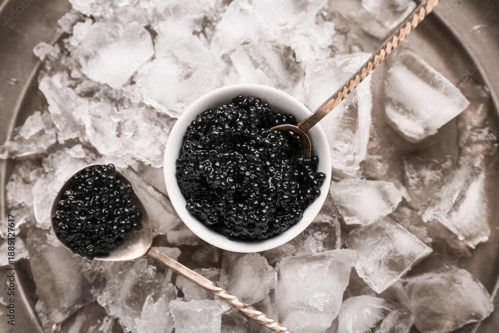 Fototapeta premium Bowl of delicious black caviar with spoon and ice cubes on tray, top view