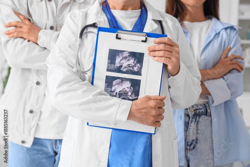 Female fertility doctor with sonogram image after IVF and young couple in clinic
