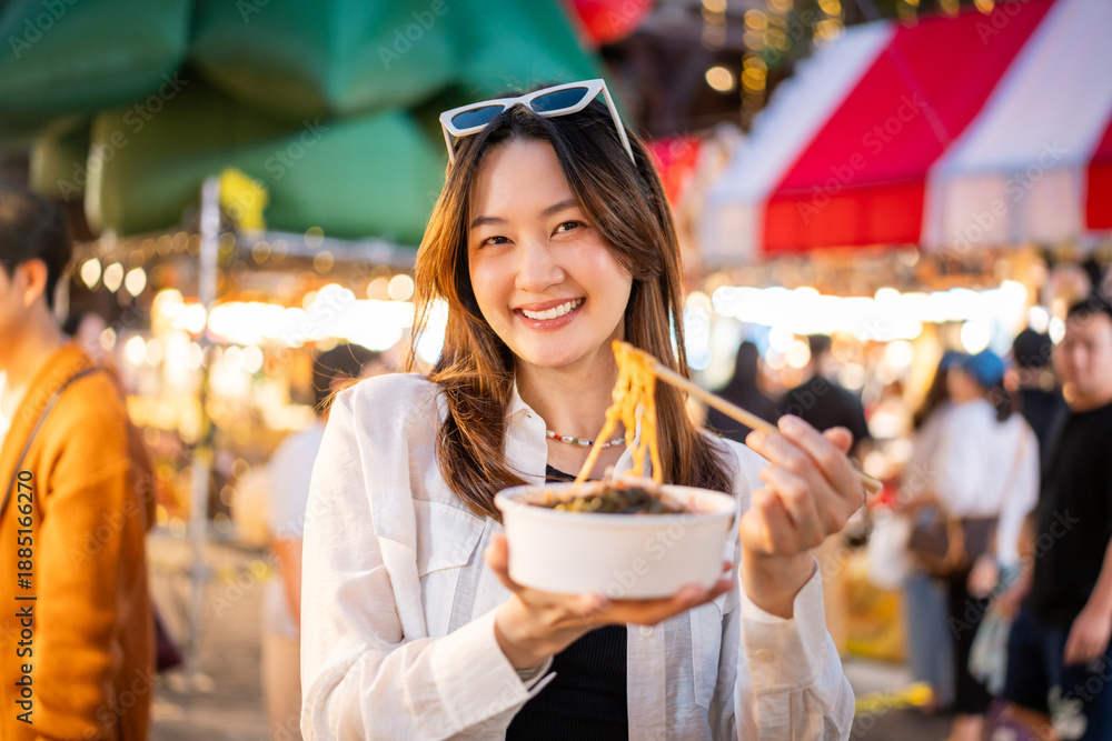 Fototapeta premium Asian woman enjoy eating street food at night market. Traveler Asian blogger women Happy tourists Beautiful female with Traditional food local road at thailand bangkok city.