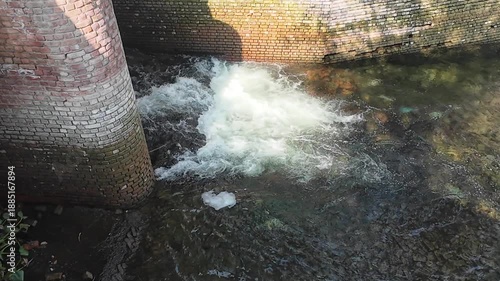Industrial Water Management System Featuring an Iron Dam Structure and Turbulent Flowing Water Against a Weathered Brick Wall