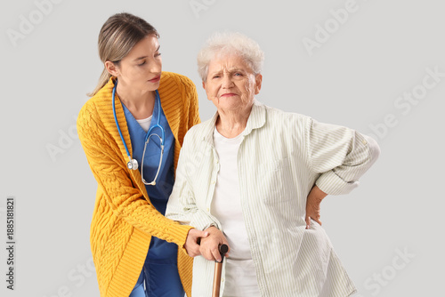 Senior woman with back pain and nurse on light background