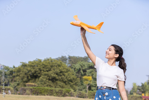 Happy young indian girl kid holding toy airplane outdoor in summer park, childhood. Future dreams, aspiration. Freedom.