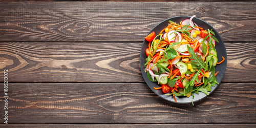 Fresh salad with vegetables. Arugula, spinach, cucumbers, tomato, onions carrots, corn andradishes in a plate on the table. Diet nutrition. Top view. Copy space