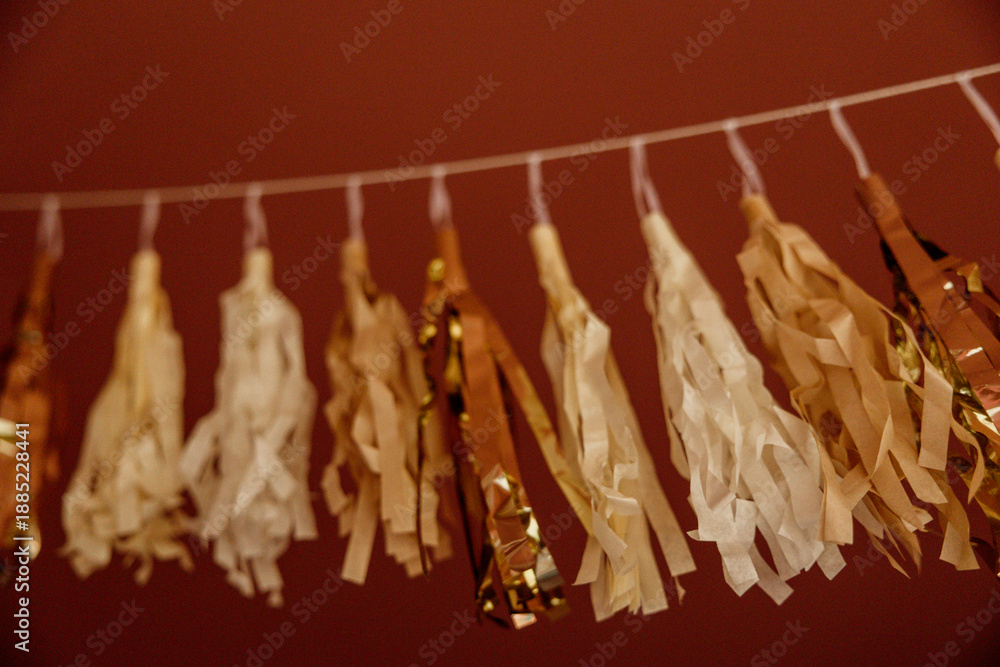 Fototapeta premium Gold and cream tassel garland hanging against a red wall.