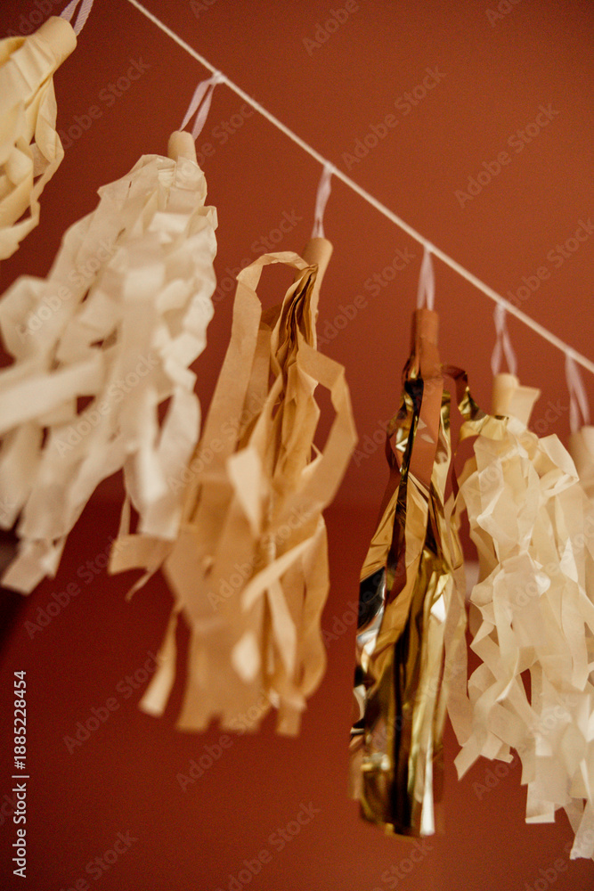 Fototapeta premium Gold and cream tassel garland hanging against a red wall.