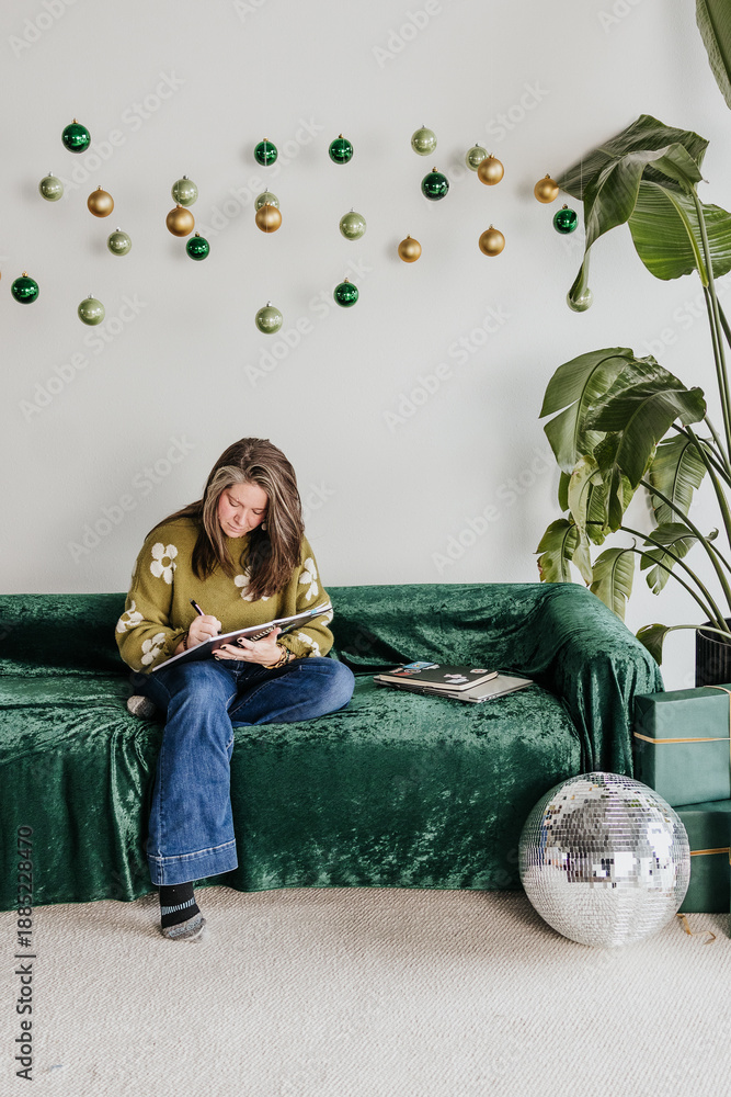 Obraz premium Woman sits on velvet covered couch writing in notebook