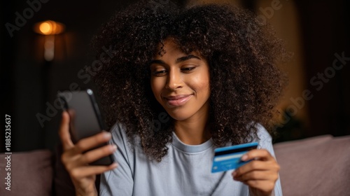 Young woman using smartphone and holding a credit card in living room during evening hours
