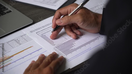Close-up of a person's hand pointing and ticking items on a business document with a pen, reviewing data and forms