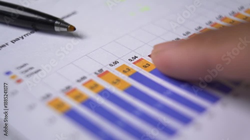 Close up view of a person pointing to financial data and bar charts on a document with a pen