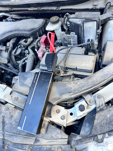 Wallpaper Mural Portable car jump starter connected to vehicle battery under open hood, emergency power supply used for engine start, automotive maintenance and roadside assistance concept. Torontodigital.ca