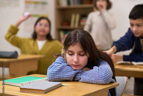Fotografija Caucasian preteen girl sitting at desk with head resting on arms appearing sad,