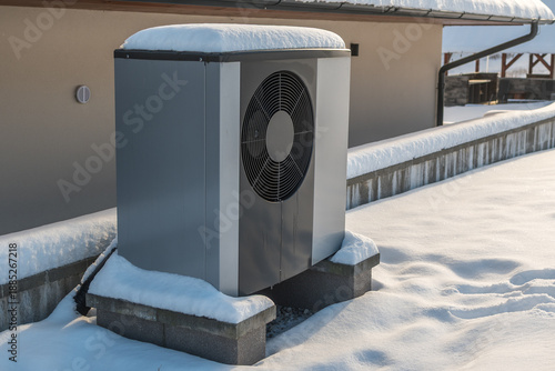 Outdoor air source heat pump unit installed beside residential building in winter conditions.