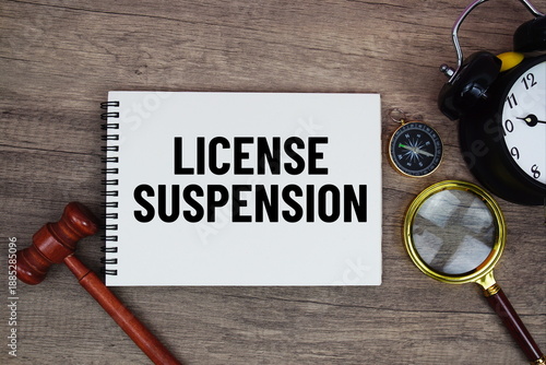 License Suspension message written on notepad with alarm clock, wood gavel and magnifying glass flat lay on wooden background