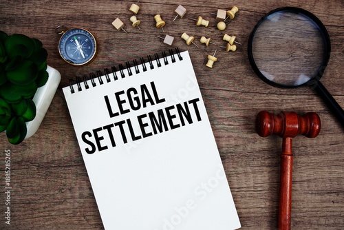 Legal Settlement message written on notepad with wood gavel and magnifying glass flat lay on wooden background