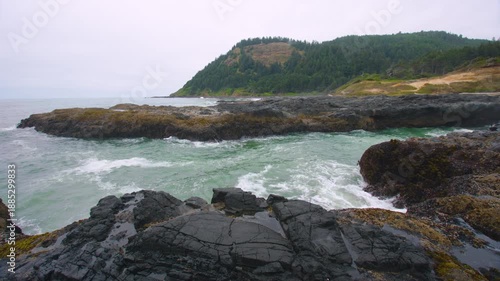 Scenic 4K stock footage captures the dramatic and powerful natural beauty of the Oregon Coast. Large, frothy waves from the Pacific Ocean rush into a narrow, rocky inlet at Cook's Chasm, part of the C