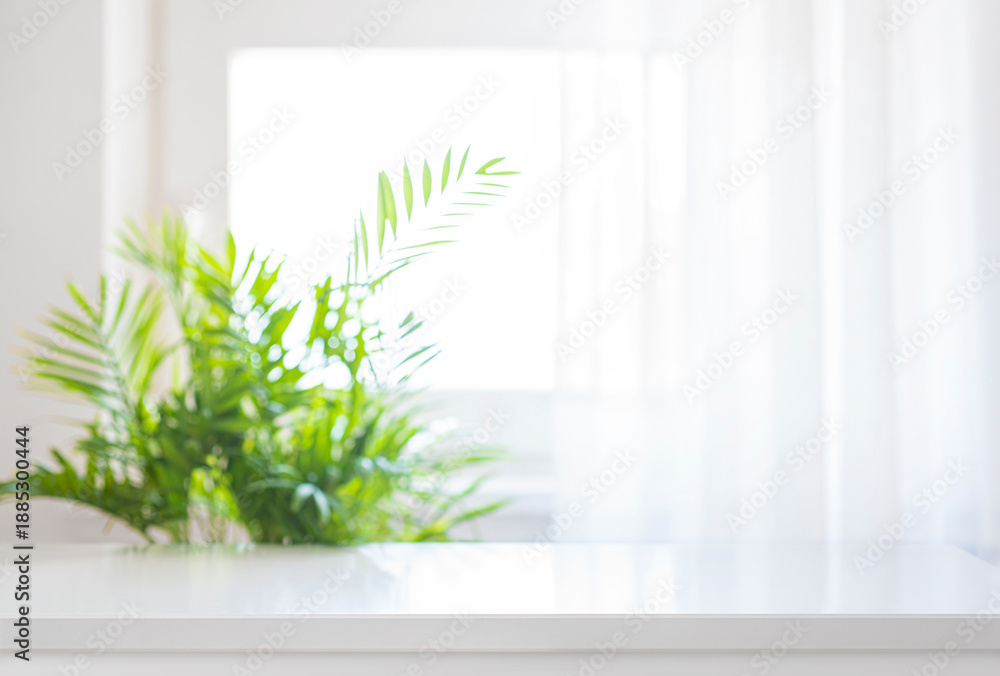 Fototapeta premium Product display background with empty white glossy table top on deeply blurred window curtain and green tropical plant leaves