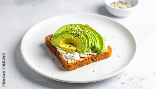 A close-up shot of a single piece of avocado toast with a creamy spread and seeds on a white plate, ready to eat.